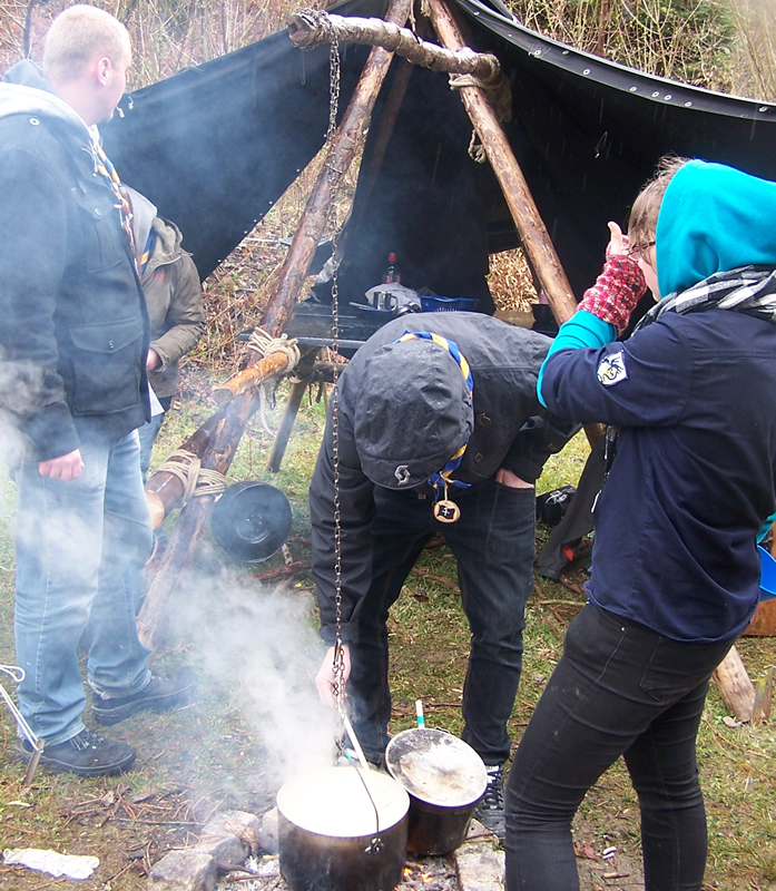Junge Kurs-Teilnehmerinnen und -Teilnehmer beim Kochen auf dem Feuer